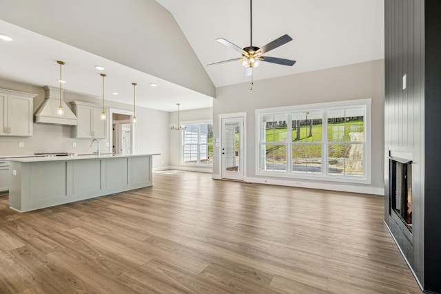 unfurnished living room featuring light wood finished floors, a large fireplace, recessed lighting, ceiling fan with notable chandelier, and high vaulted ceiling