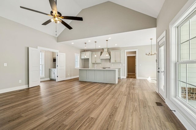 unfurnished living room with light wood finished floors, visible vents, baseboards, ceiling fan with notable chandelier, and high vaulted ceiling