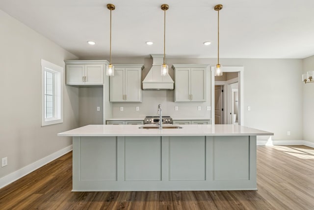 kitchen featuring custom exhaust hood, a center island with sink, light countertops, and a sink