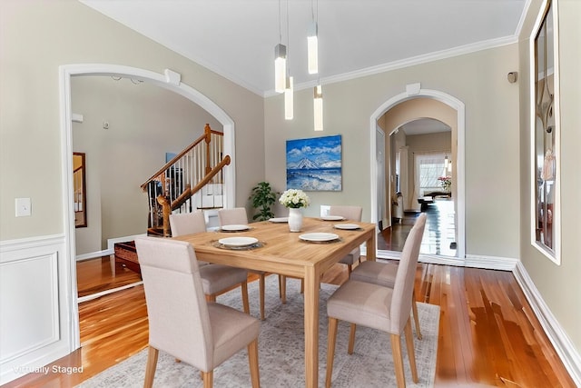 dining area with stairway, arched walkways, ornamental molding, and light wood-style flooring