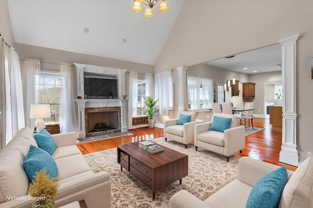 living room with a fireplace, ornate columns, light wood-style flooring, and a wealth of natural light