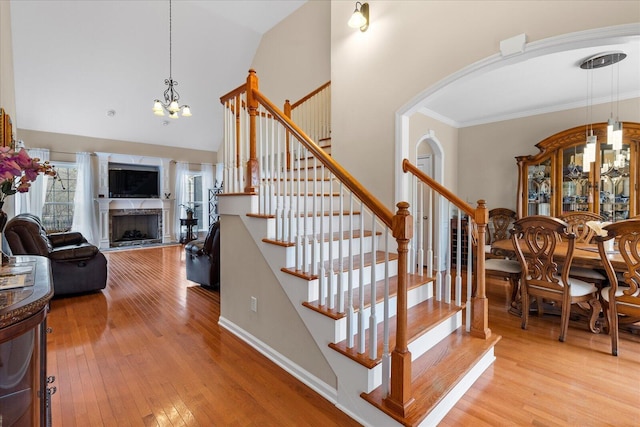 staircase with an inviting chandelier, a fireplace, arched walkways, high vaulted ceiling, and wood finished floors