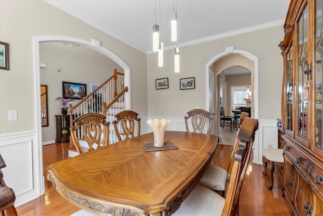 dining room featuring light wood finished floors, arched walkways, a wainscoted wall, ornamental molding, and stairway