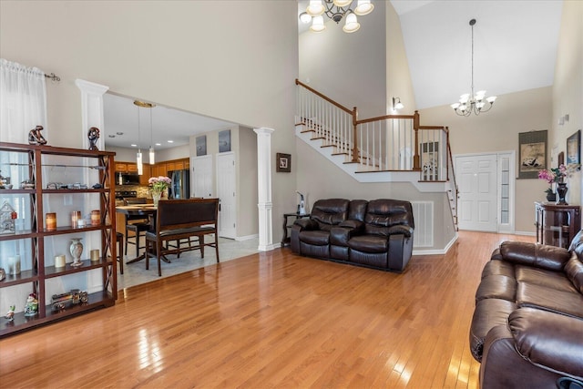 living area featuring light wood-style floors, stairs, a notable chandelier, and high vaulted ceiling