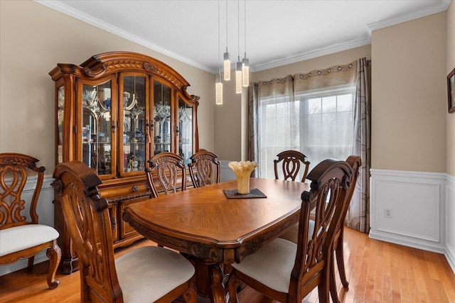 dining area with wainscoting, ornamental molding, and light wood-style floors