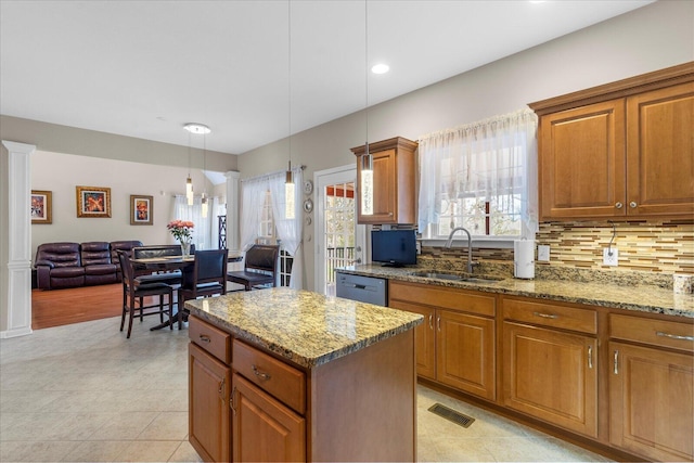 kitchen with a sink, dishwashing machine, brown cabinets, and light stone countertops
