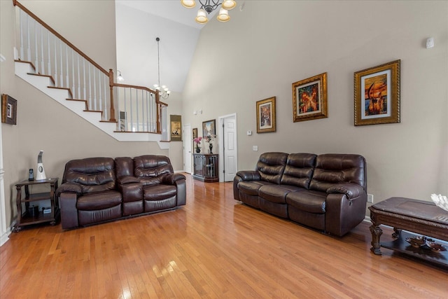 living area featuring stairs, a chandelier, light wood-style flooring, and a towering ceiling