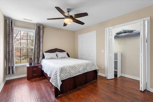 bedroom with ceiling fan, visible vents, baseboards, dark wood-style floors, and multiple closets