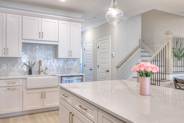 kitchen with pendant lighting, a sink, light stone counters, stainless steel dishwasher, and white cabinetry