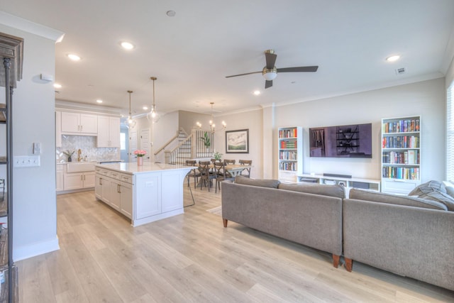 living room featuring stairway, light wood-style flooring, recessed lighting, and ceiling fan with notable chandelier