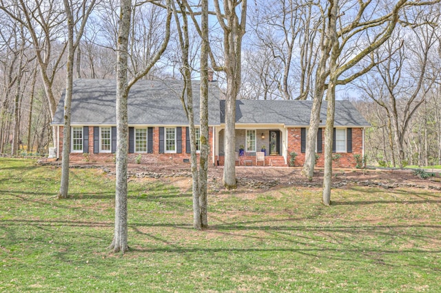 view of front of house with brick siding, covered porch, a front yard, and roof with shingles