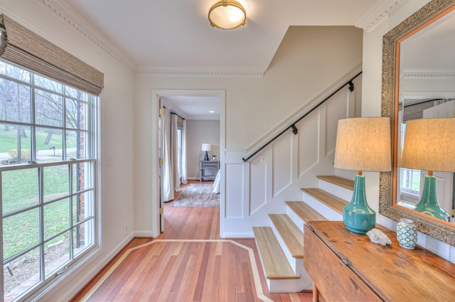 foyer featuring a decorative wall, crown molding, stairs, and light wood-style floors