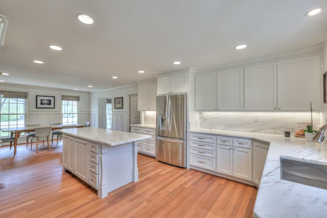 kitchen with a center island, decorative backsplash, light wood-style flooring, stainless steel fridge, and a sink