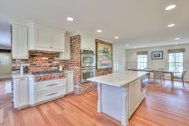 kitchen featuring a wainscoted wall, appliances with stainless steel finishes, white cabinets, and light wood-style flooring