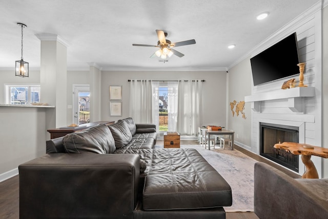 living area with a ceiling fan, a large fireplace, crown molding, baseboards, and dark wood-style flooring