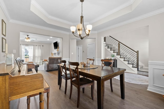 dining space with a tray ceiling, wood finished floors, crown molding, and stairway