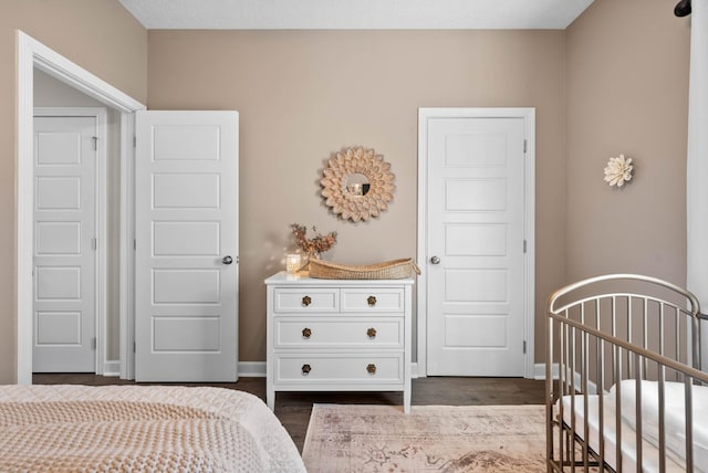 bedroom featuring baseboards, dark wood-type flooring, and a nursery area