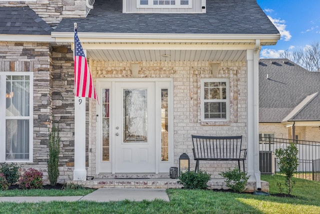 doorway to property featuring stone siding, roof with shingles, covered porch, and fence