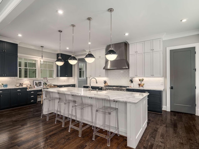 kitchen featuring dark wood-type flooring, a large island, a sink, a breakfast bar area, and wall chimney range hood