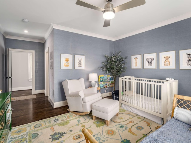 bedroom featuring wood finished floors, a nursery area, crown molding, wallpapered walls, and baseboards