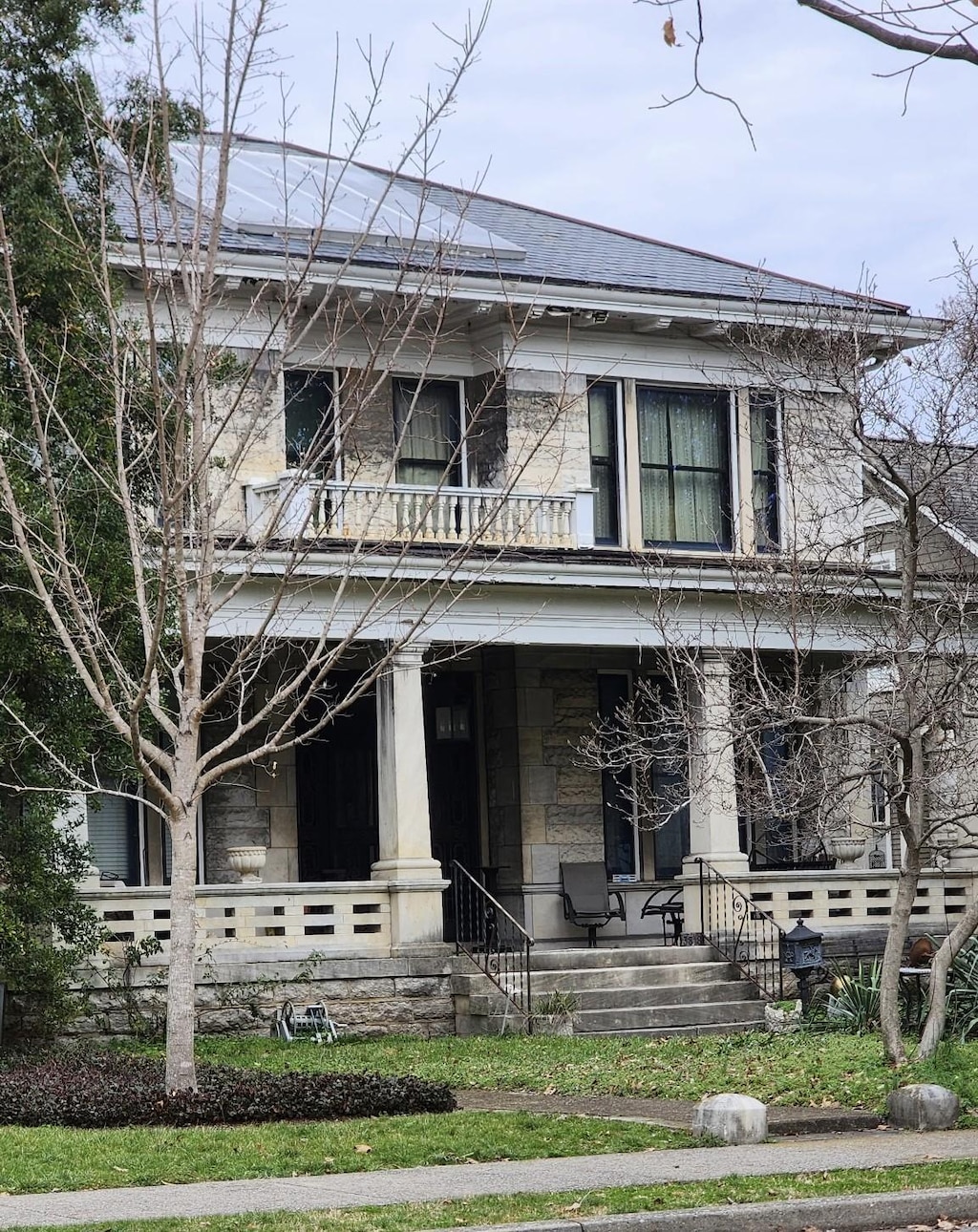 view of front facade featuring stone siding, a balcony, covered porch, and a shingled roof