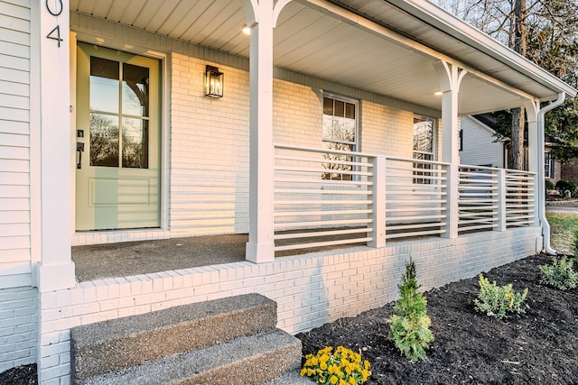 view of exterior entry featuring brick siding and a porch