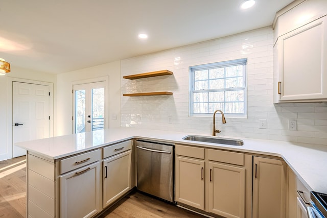 kitchen featuring light wood finished floors, dishwasher, light countertops, a peninsula, and a sink