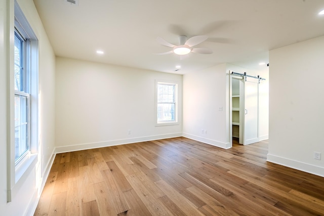 spare room featuring a barn door, wood finished floors, baseboards, and ceiling fan