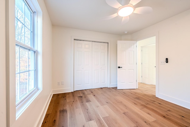 unfurnished bedroom featuring light wood-style flooring, multiple windows, baseboards, and a closet