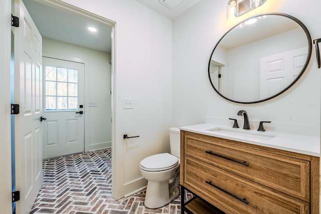 bathroom with toilet, vanity, and brick floor