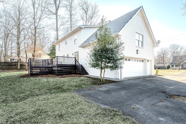 view of home's exterior featuring an attached garage, fence, a wooden deck, a lawn, and driveway