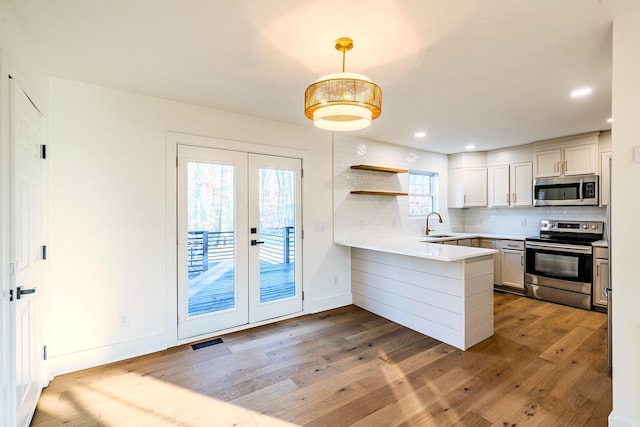 kitchen with visible vents, a peninsula, stainless steel appliances, french doors, and tasteful backsplash