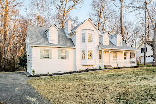 view of front of house with aphalt driveway, covered porch, a front yard, a shingled roof, and a chimney