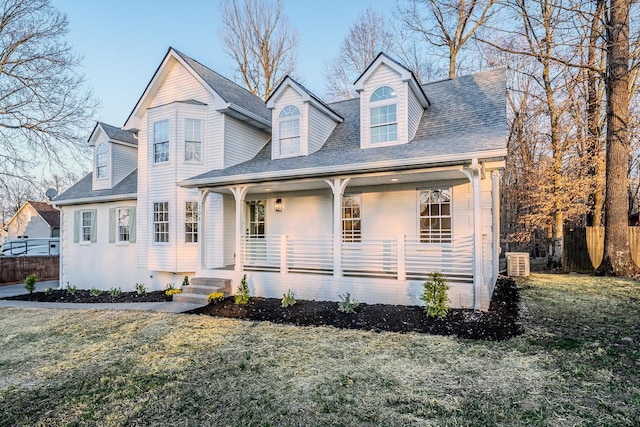 view of front of house with a porch, a shingled roof, a front yard, and fence