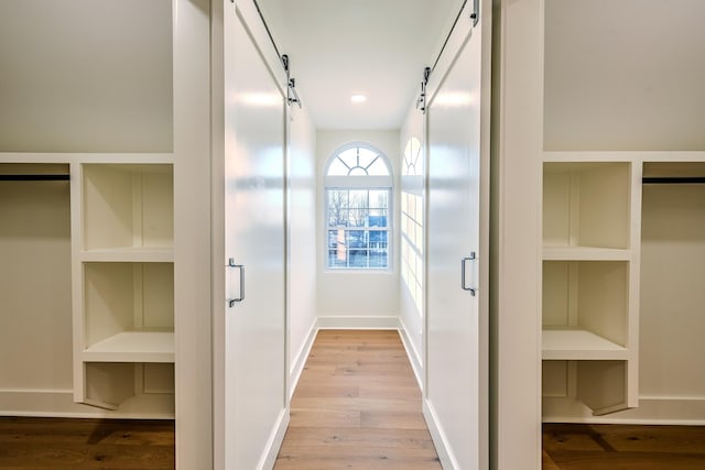 corridor with light wood finished floors, built in shelves, and baseboards