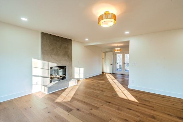 unfurnished living room featuring hardwood / wood-style flooring, french doors, baseboards, and a large fireplace