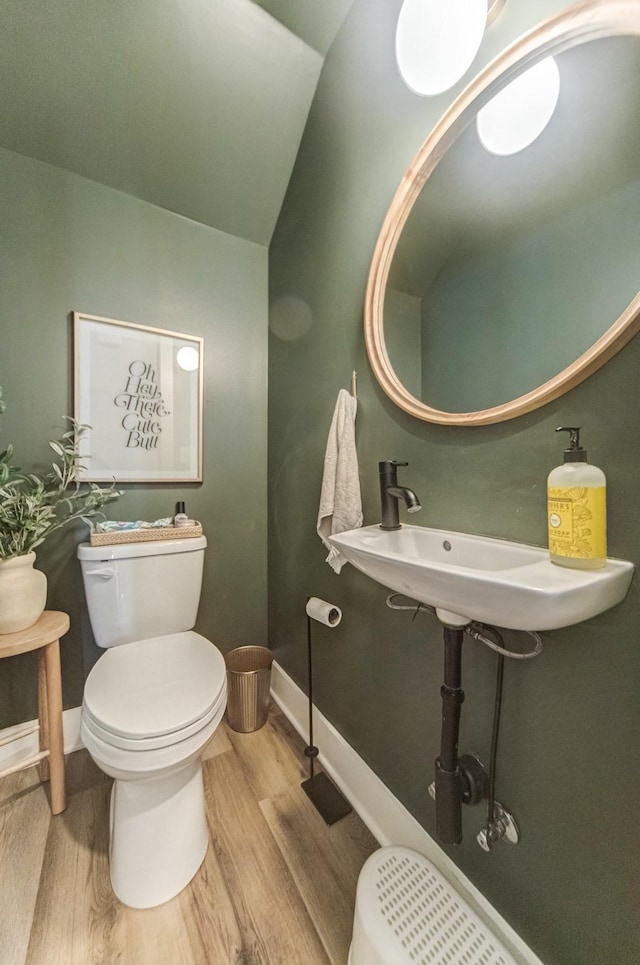 half bath with wood finished floors, baseboards, lofted ceiling, a sink, and toilet