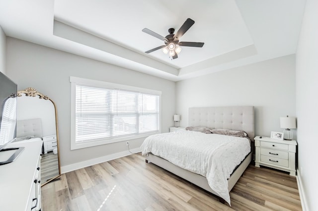 bedroom with ceiling fan, baseboards, a raised ceiling, and light wood-style floors