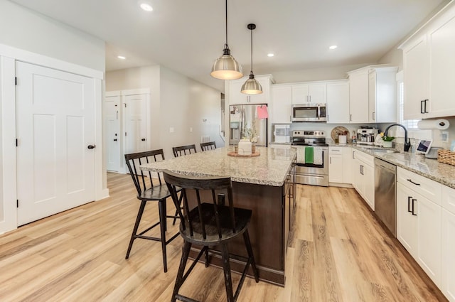 kitchen with a sink, appliances with stainless steel finishes, a breakfast bar area, white cabinets, and light wood finished floors