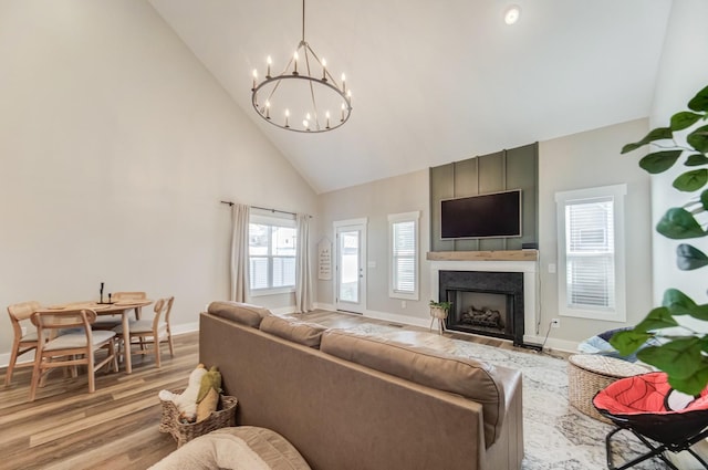 living area with baseboards, high vaulted ceiling, an inviting chandelier, light wood-style flooring, and a fireplace