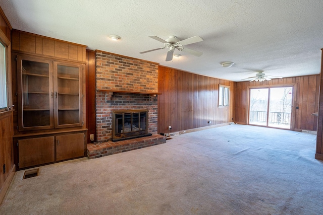 unfurnished living room featuring carpet flooring, a ceiling fan, visible vents, and wood walls