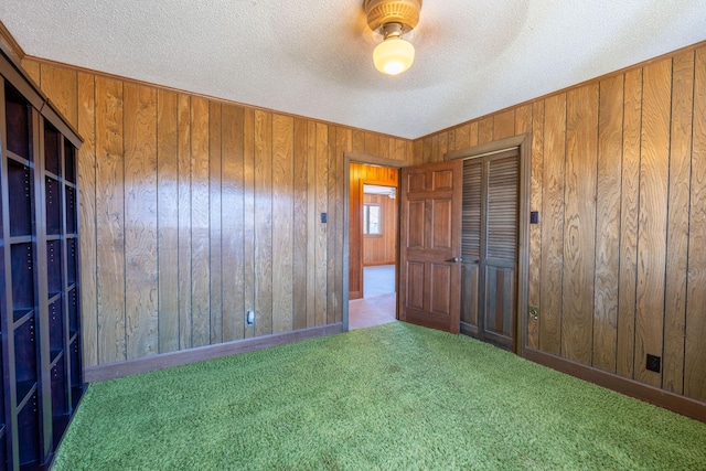 unfurnished bedroom featuring a textured ceiling, a closet, wooden walls, carpet, and ceiling fan