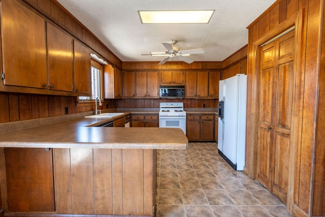 kitchen featuring white appliances, a peninsula, ceiling fan, a sink, and brown cabinets