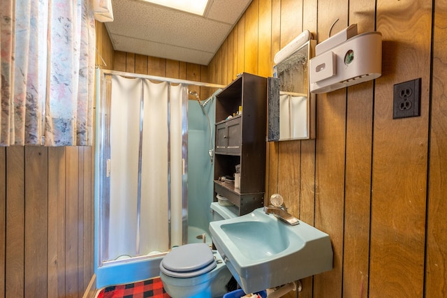 bathroom with toilet, a sink, a drop ceiling, wooden walls, and a shower stall