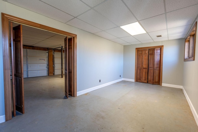 unfurnished bedroom with a paneled ceiling, baseboards, and concrete flooring