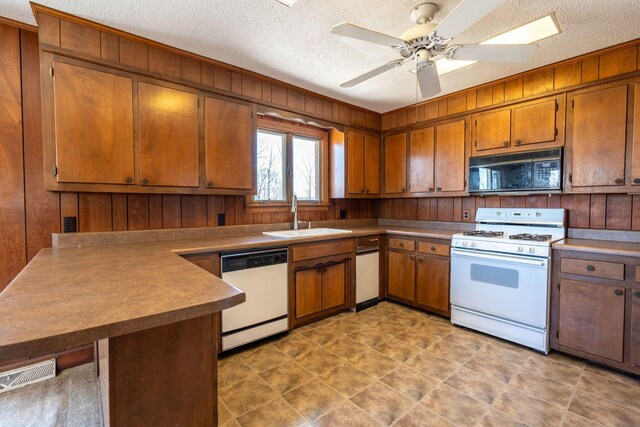 kitchen with a sink, white appliances, a peninsula, and wood walls