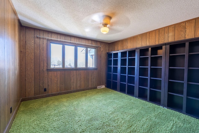 unfurnished room with visible vents, wood walls, and carpet flooring