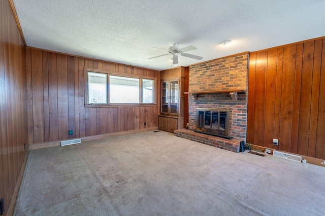 unfurnished living room with a ceiling fan, visible vents, carpet floors, a textured ceiling, and a brick fireplace