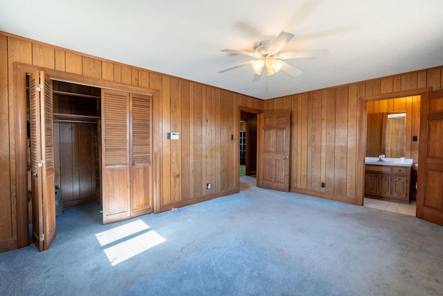unfurnished bedroom with a ceiling fan, ensuite bath, a closet, wooden walls, and carpet flooring