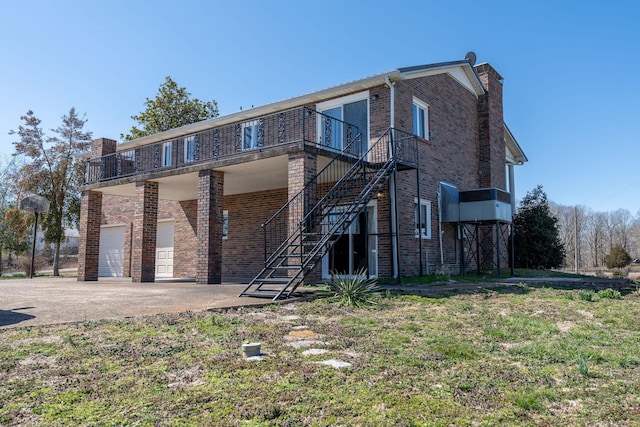 rear view of property with driveway, a chimney, stairs, a garage, and brick siding